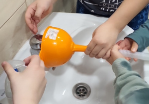 Dzieci próbują nalewać wodę za pomocą lejka.